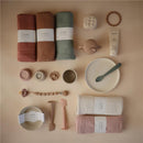 Mushie Extra Soft Baby Blanket in ivory, alongside additional baby items like bowls, spoons, and toys in soft colors.