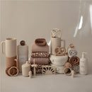 Mushie Extra Soft Baby Blanket in ivory, surrounded by various baby products in soft, neutral tones, including towels and accessories.