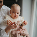 Mushie 2-Pack Finger Toothbrush in Shifting Sand and Blush colors, displayed with a baby holding one while seated.