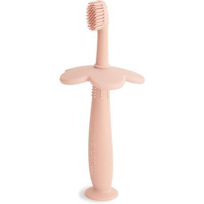 Mushie silicone flower training toothbrush in blush color, designed for young children with a textured handle and bristles.
