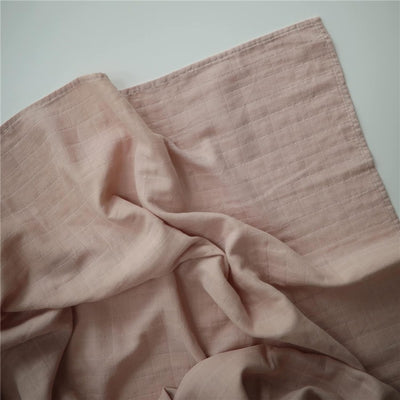 Muslin swaddle blanket in blush color, featuring a soft, textured fabric with a subtle grid pattern.