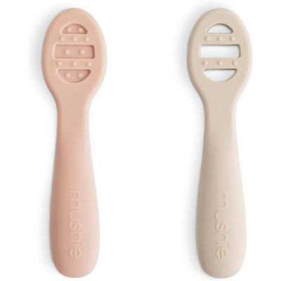 Mushie silicone baby spoons in blush and shifting sand colors, designed for first feeding, featuring textured grips.