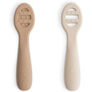 Silicone baby spoons in natural and shifting sand colors, designed for first feeding, featuring textured grips.