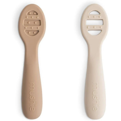 Silicone baby spoons in natural and shifting sand colors, designed for first feeding, featuring textured grips.