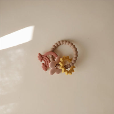 Mushie Silicone Nature Teething Ring features soft, colorful shapes including a rainbow, flower, and star on a textured ring.