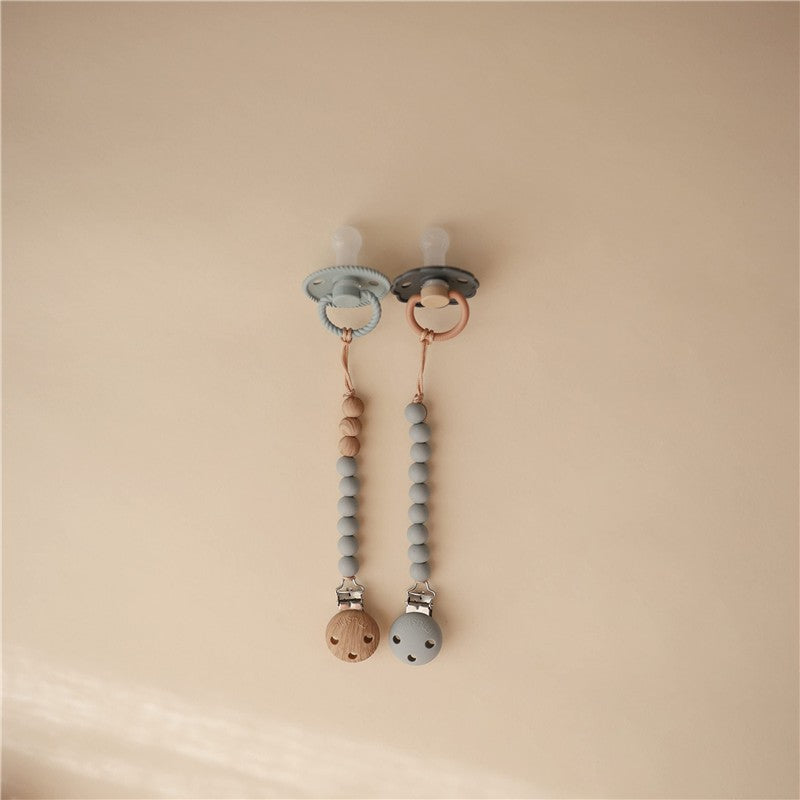 Mushie Eva Pacifier Clip in stone color, featuring two clips with wooden and silicone beads attached to pacifiers.