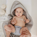 Baby lying on a soft surface in a gray hooded towel, wearing a striped diaper, and holding a pacifier clip attached to a pacifier.