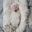 Mushie Eva Pacifier Clip in Stone attached to a sleeping baby swaddled in soft, neutral-toned fabrics.