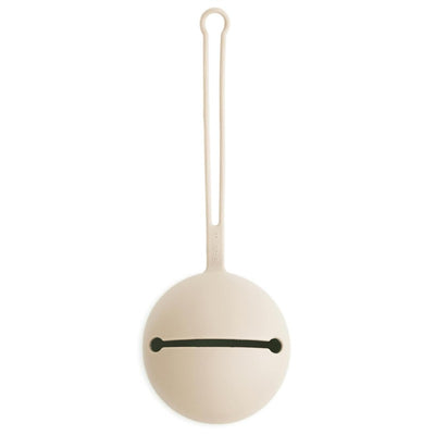 Mushie silicone pacifier holder case in Shifting Sand color, featuring a round body, a black slot, and a looped handle.