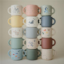 Colorful stack of Mushie silicone snack cups featuring playful designs including animals and patterns, suitable for kids.