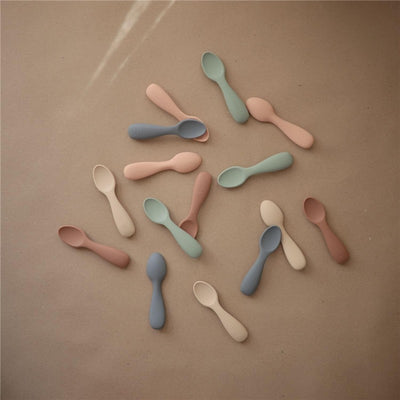 Silicone toddler starter spoons in Cambridge Blue and Shifting Sand colors, featuring soft, ergonomic designs.