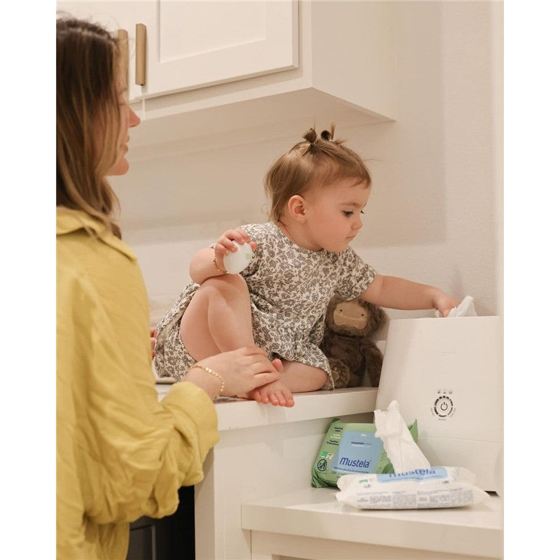 Toddler sitting on a counter, reaching for Mustela Compostable Cleansing Water Wipes next to a white wipe dispenser.