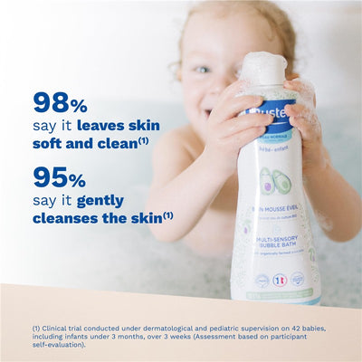 Mustela Multi-Sensory Bubble Bath bottle held by a child in a bath, with claims about skin softness and cleansing.