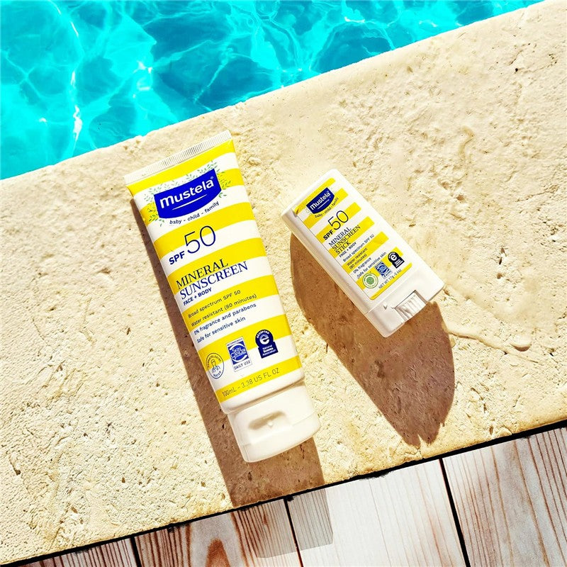 Mustela SPF 50 Mineral Sunscreen Stick and tube on a stone surface by a pool, features yellow and white packaging.