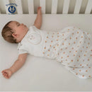 Soft pink Nested Bean Zen Sack Classic for infants, featuring a smiling face design, worn by a sleeping baby in a crib.