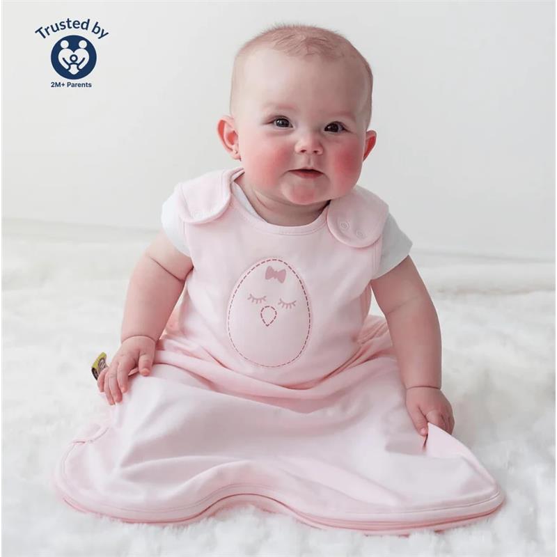 Soft pink Nested Bean Zen Sack Classic with a cute chick design, worn by a smiling baby sitting on a fluffy surface.