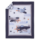 Mini crib bedding set featuring colorful airplanes, clouds, and stars on a white background with a navy border.