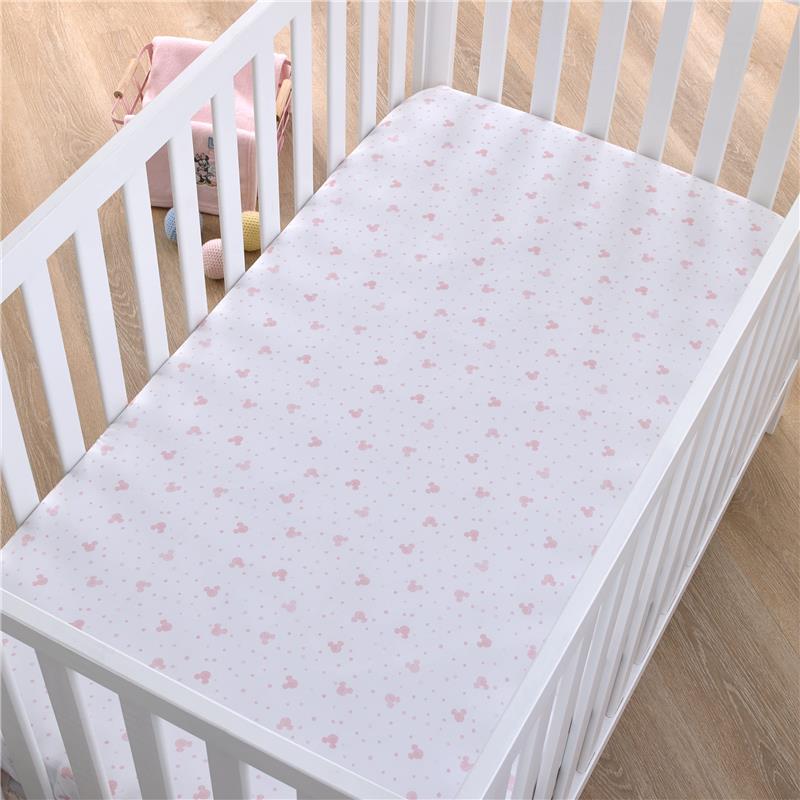 Fitted crib sheet featuring a pink polka dot design with Minnie Mouse icons, placed in a white crib.