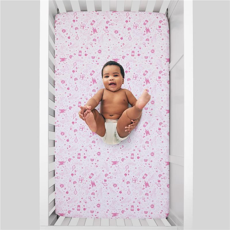Fitted crib sheet featuring a white and pink design with castles, hearts, and stars, occupied by a smiling baby.