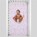 Fitted crib sheet featuring a white and pink design with castles, hearts, and stars, occupied by a smiling baby.