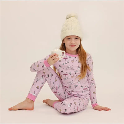 Girl wearing a pink long-sleeve pajama set with winter-themed patterns, holding a cup of hot chocolate.