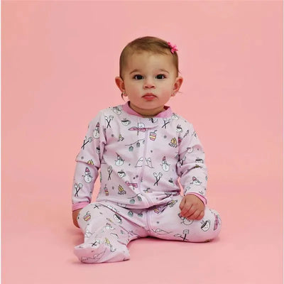 Toddler wearing a pink Noomie Apres Ski Zipper Footie with playful winter-themed patterns, seated against a pink backdrop.