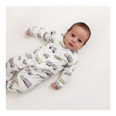 Baby boy wearing the Noomie transportation zipper footie, featuring a pattern of various vehicles on a white background.