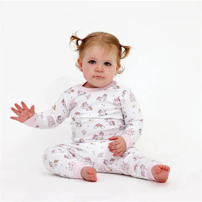 Baby girl wearing a pink and white unicorn-themed long sleeve pajama set, sitting and waving.