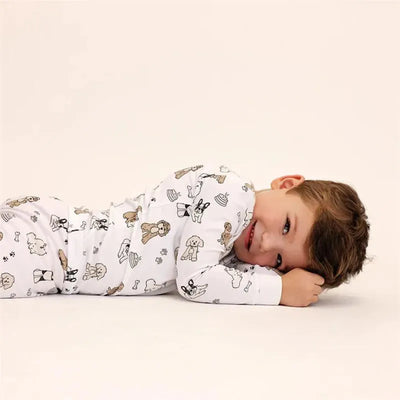 Long sleeve pajama set for kids featuring cute dog illustrations, modeled by a smiling child lying on his stomach.