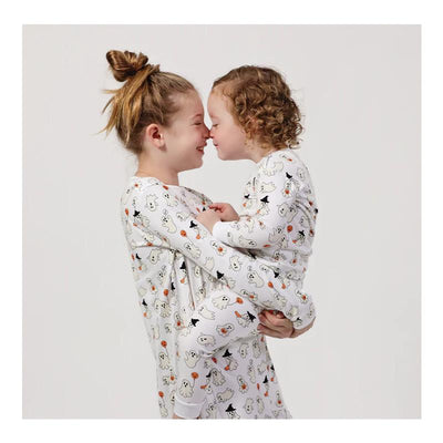 Two children in matching Noomie Happy Ghosts long sleeve pajama sets share a close moment, smiling and leaning their foreheads together.