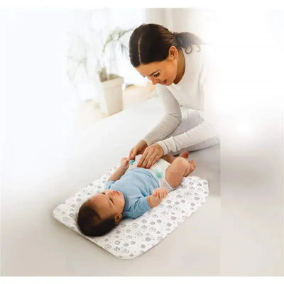 A caregiver gently changes a baby on a Nuby Dr Talbots disposable changing pad, featuring a playful pattern.