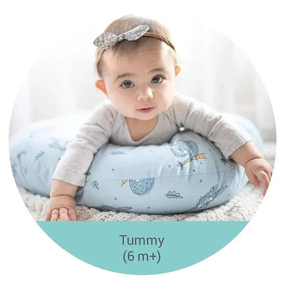 Baby lying on a Nuby Dr Talbots white nursing pillow with a blue pattern, preparing for tummy time.