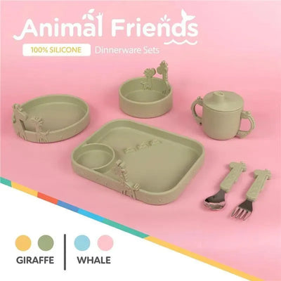 Green silicone dinnerware set featuring giraffe-themed plates, bowl, cup, and utensils on a pink background.