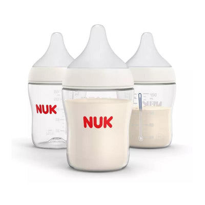 Three Nuk 5 oz baby bottles with white nipples, one transparent, and two with cream-colored contents and measurement markings.