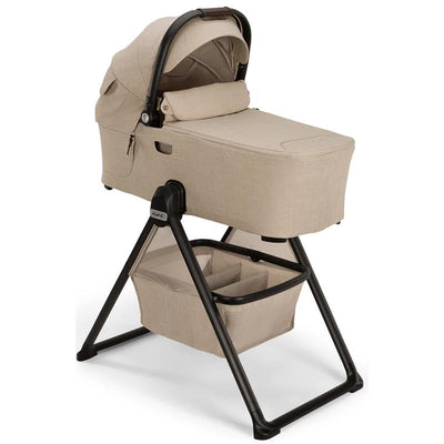 Nuna DEMI™ next Bassinet + Stand in Biscotti color, featuring a soft fabric exterior, adjustable canopy, and storage basket below.