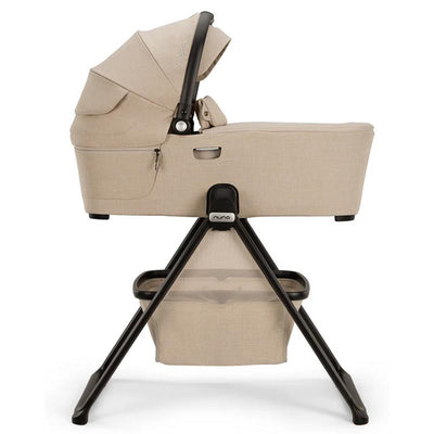 Nuna DEMI™ next Bassinet in Biscotti color, featuring a modern design with a sturdy black stand and storage basket underneath.