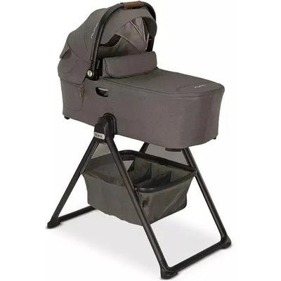 Nuna DEMI™ next Bassinet in Granite with a dark gray fabric, elevated on a black stand with a lower storage basket.