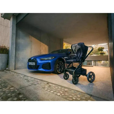 Nuna MIXX™ next Stroller with Magnetic Buckle in black, positioned beside a blue BMW in a modern garage setting.