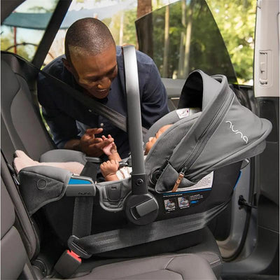 Nuna PIPA™ rx infant car seat in cedar with RELX base, secured in a vehicle while a man interacts with a baby inside.