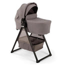 Nuna SWIV & TRIV Series Bassinet in Umber color with a removable stand and storage basket underneath.