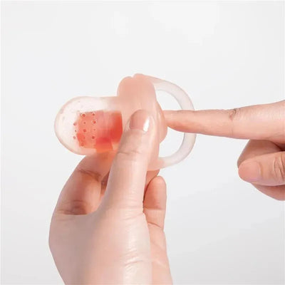 Silicone fruit feeder with a finger inserted, demonstrating its use for introducing solid foods to babies.