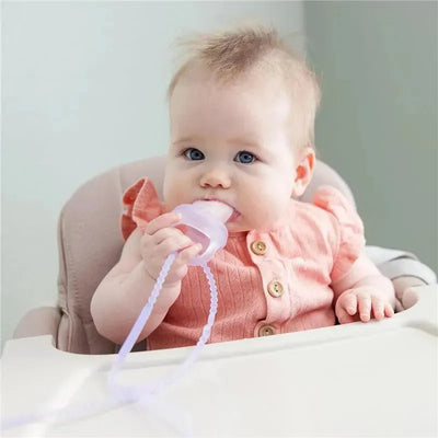 Baby sitting in a high chair holds a silicone strap teething toy in pink, exploring it with her mouth.