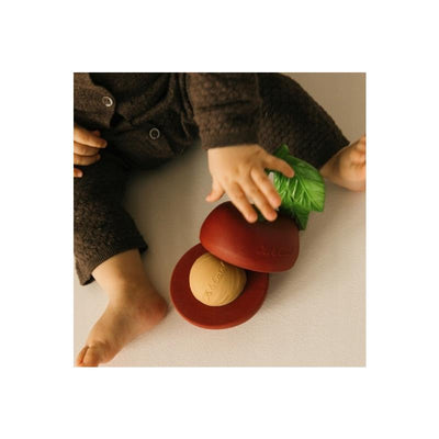 Cherry stacking toy and rattle ball by Oli & Carol, featuring red cherries and green leaf, held by a child.