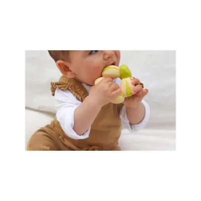 Baby chewing on the Oli & Carol Patricio La Pistache teether, which resembles a green and yellow nut.
