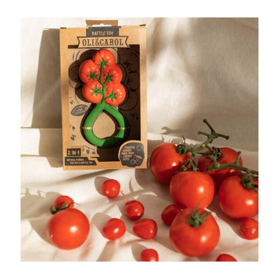 Oli & Carol Tomato Rattle Toy displayed in packaging, surrounded by fresh tomatoes, emphasizing its 2-in-1 design.