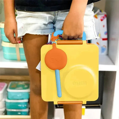 Two-pack of OmieBox reusable fork and spoon set in a yellow pod, held by a child.
