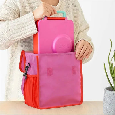 OmieBox insulated nylon lunch tote in pink with a pink container inside, being held by a person in a cozy sweater.