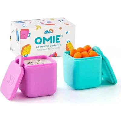 Two leakproof silicone dip containers in pink and teal, with one containing a dip and the other filled with orange snacks, next to a colorful box.