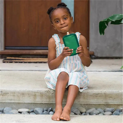 Child sitting on steps, holding a green OmieBox pouch cooler, wearing a striped outfit.