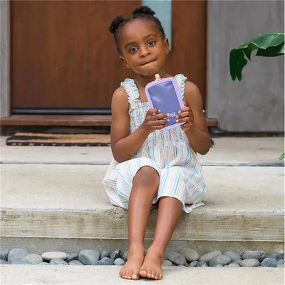 Child sitting on steps, holding a purple OmieBox pouch cooler with a textured surface, wearing a striped dress.